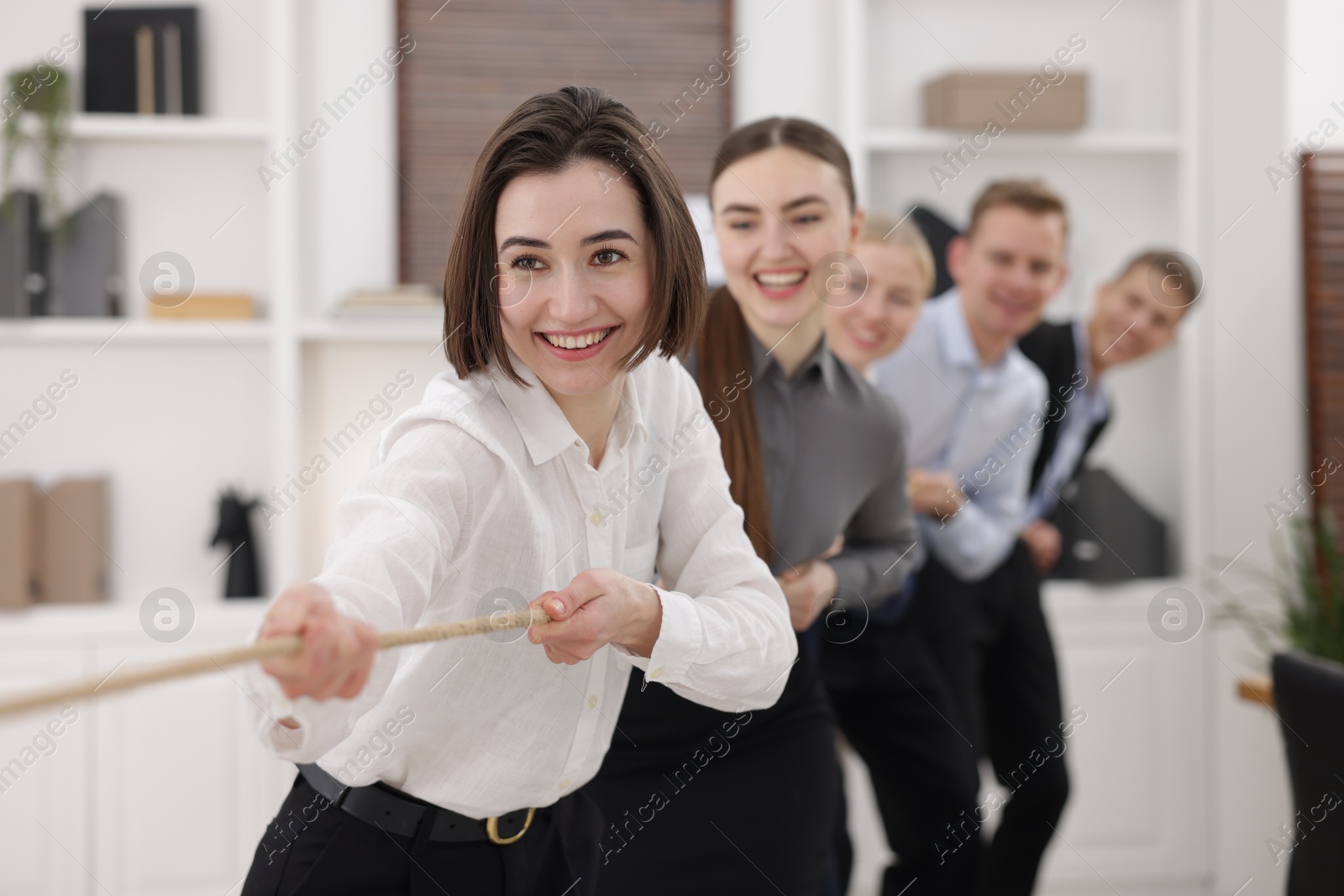 Photo of Competition concept. Group of happy businesspeople pulling rope in office, selective focus