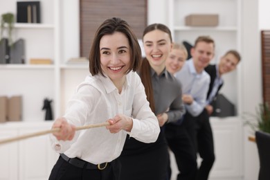 Photo of Competition concept. Group of happy businesspeople pulling rope in office, selective focus