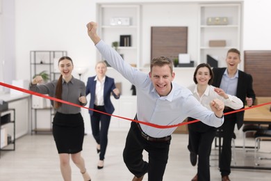 Competition concept. Happy businessman crossing red finish line ahead of his colleagues in office