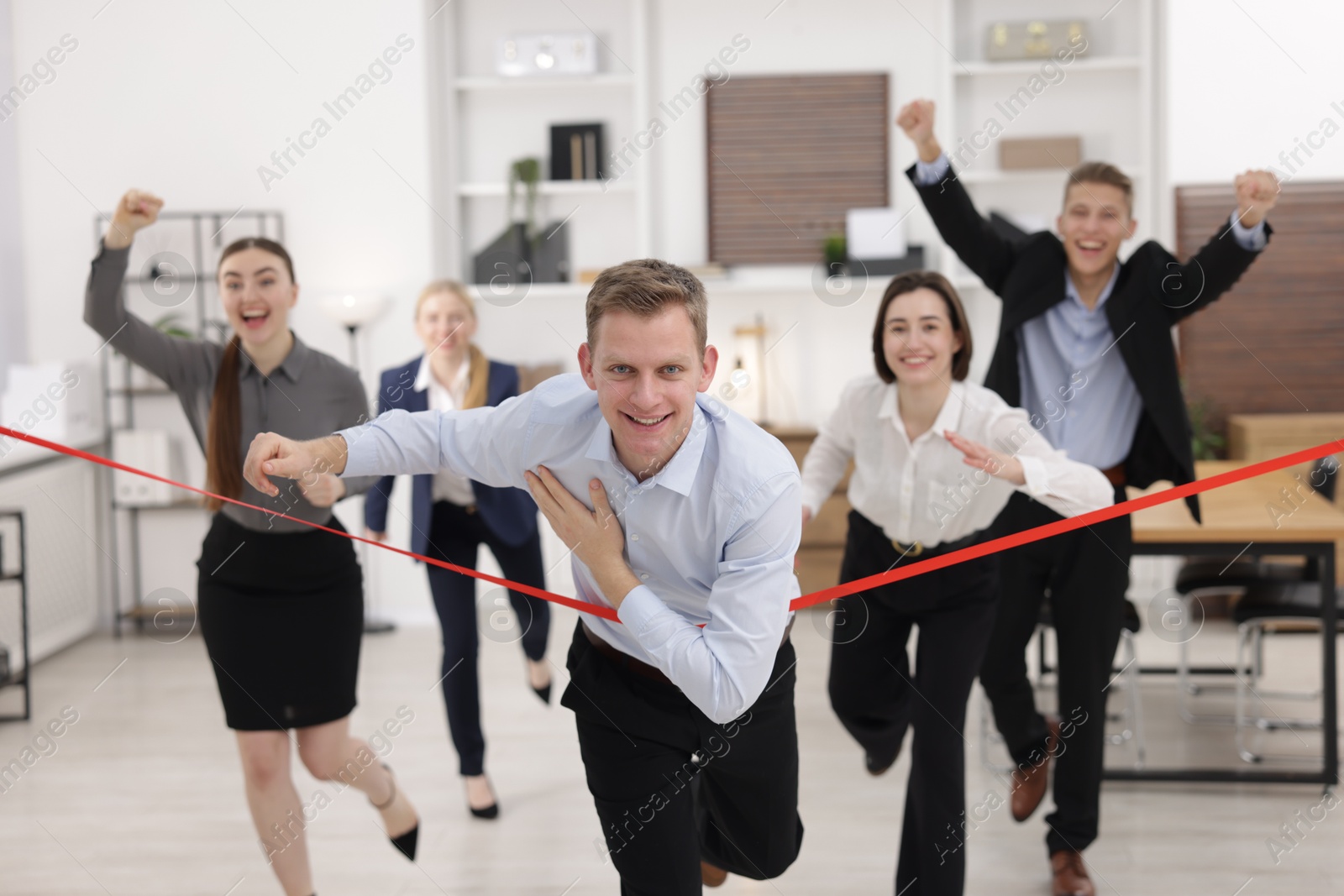 Photo of Competition concept. Happy businessman crossing red finish line ahead of his colleagues in office