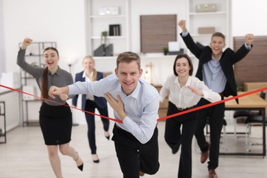 Competition concept. Happy businessman crossing red finish line ahead of his colleagues in office