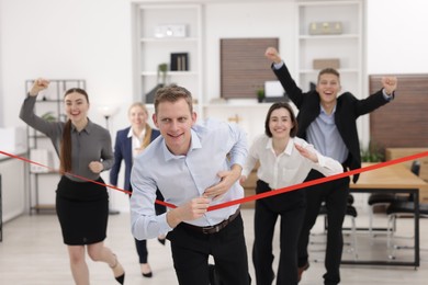 Competition concept. Happy businessman crossing red finish line ahead of his colleagues in office