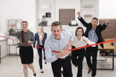 Photo of Competition concept. Happy businessman crossing red finish line ahead of his colleagues in office