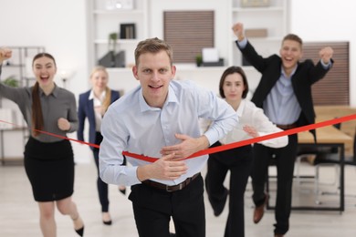 Competition concept. Happy businessman crossing red finish line ahead of his colleagues in office