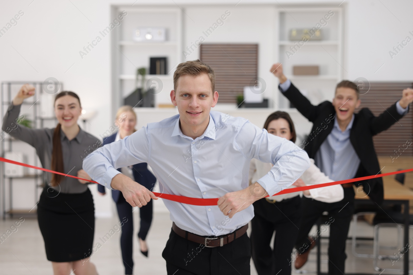 Photo of Competition concept. Happy businessman crossing red finish line ahead of his colleagues in office