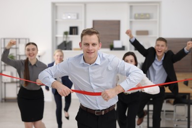 Competition concept. Happy businessman crossing red finish line ahead of his colleagues in office