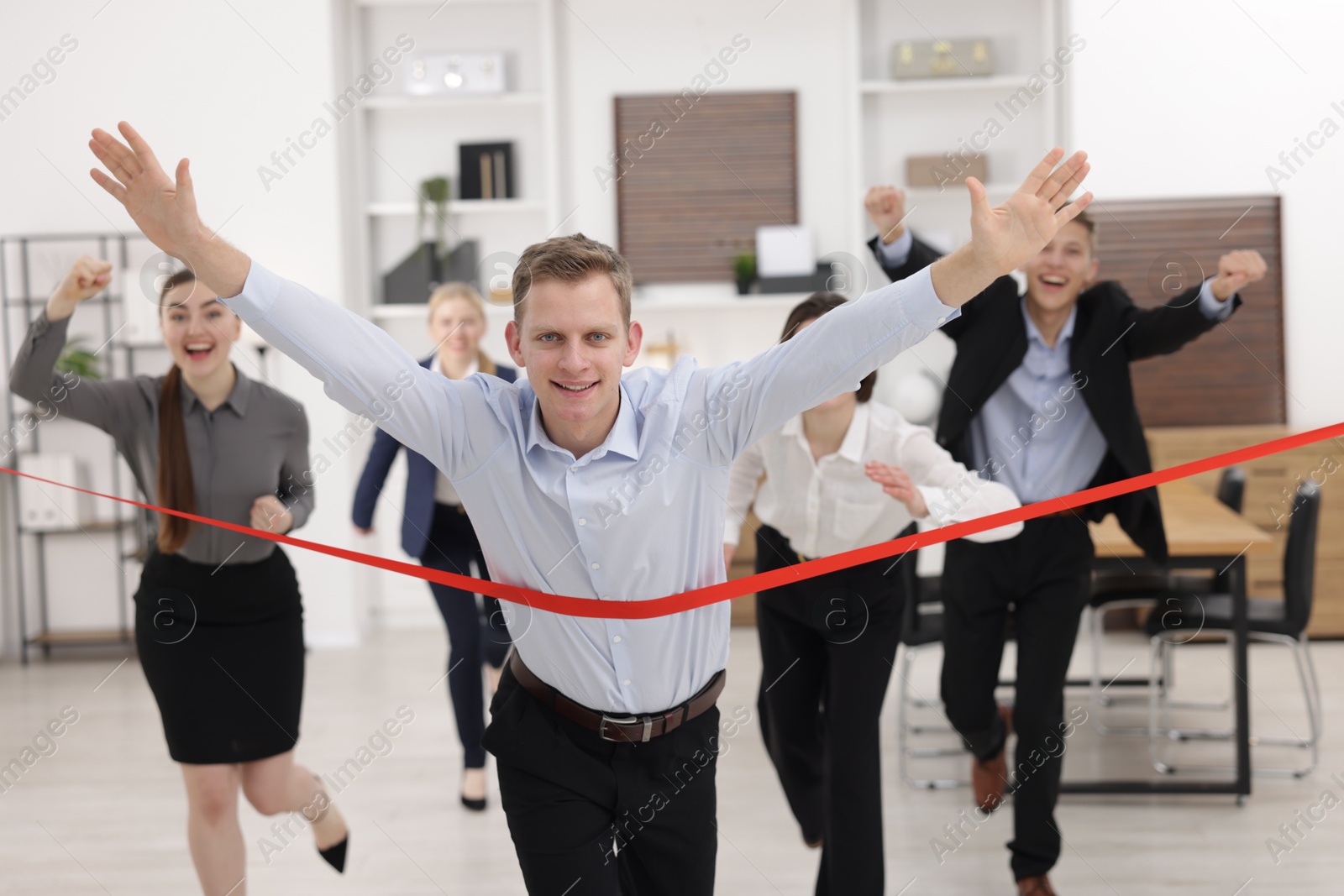 Photo of Competition concept. Happy businessman crossing red finish line ahead of his colleagues in office