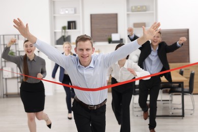 Competition concept. Happy businessman crossing red finish line ahead of his colleagues in office