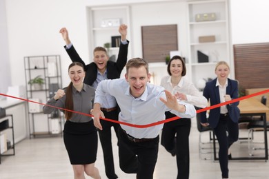 Competition concept. Happy businessman crossing red finish line ahead of his colleagues in office