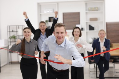 Competition concept. Happy businessman crossing red finish line ahead of his colleagues in office