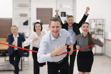 Competition concept. Happy businessman crossing red finish line ahead of his colleagues in office