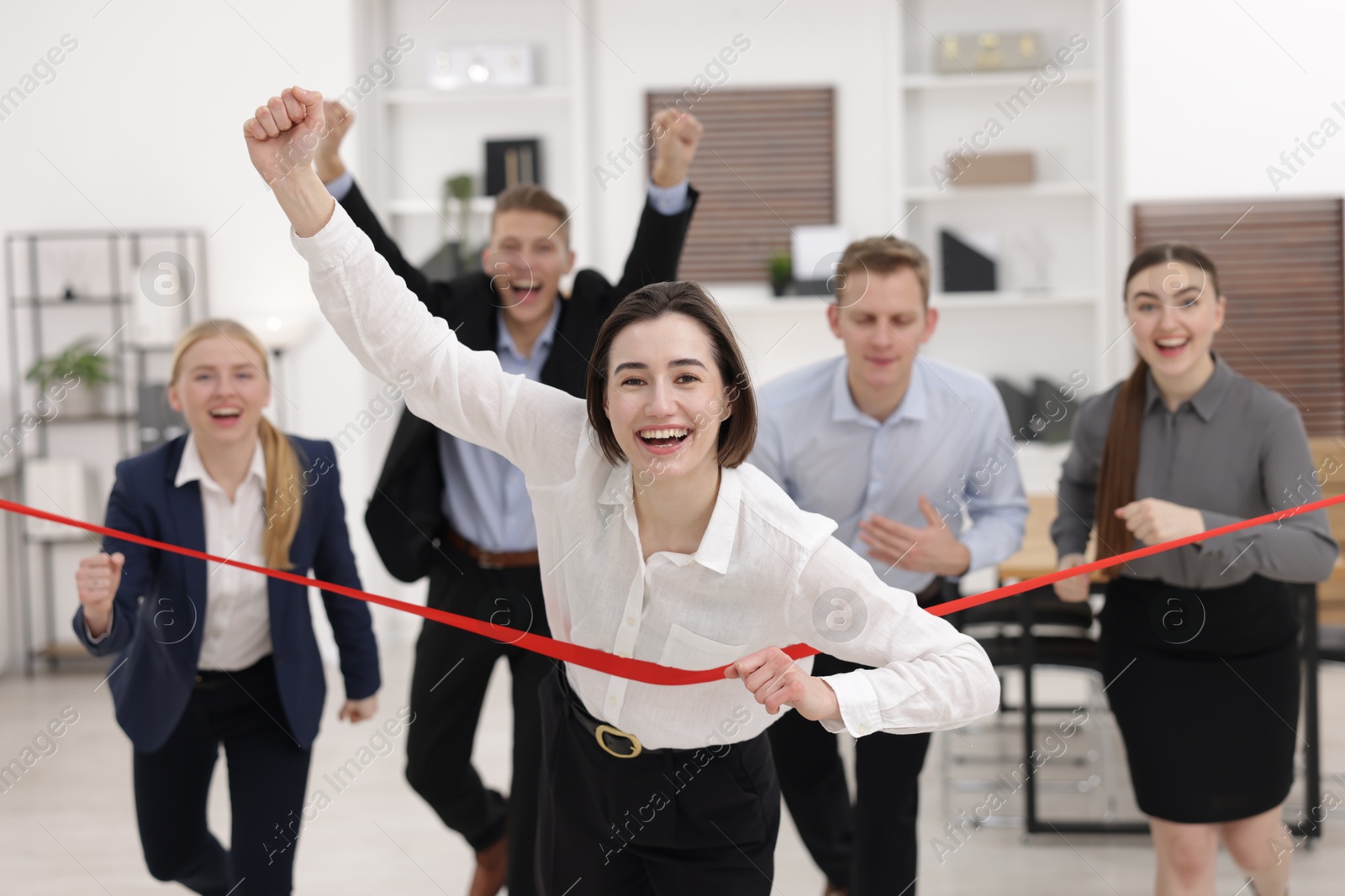 Photo of Competition concept. Happy businesswoman crossing red finish line ahead of her colleagues in office