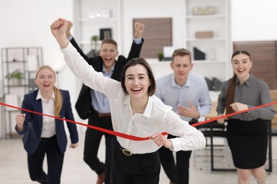 Photo of Competition concept. Happy businesswoman crossing red finish line ahead of her colleagues in office