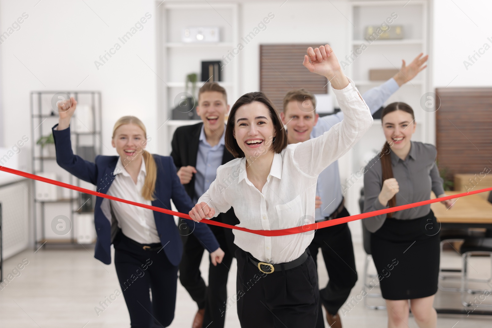 Photo of Competition concept. Happy businesswoman crossing red finish line ahead of her colleagues in office