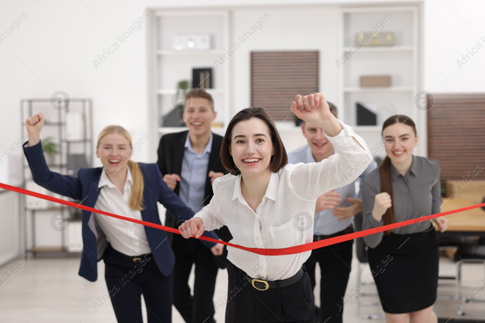 Photo of Competition concept. Happy businesswoman crossing red finish line ahead of her colleagues in office