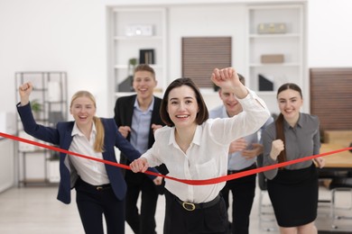 Photo of Competition concept. Happy businesswoman crossing red finish line ahead of her colleagues in office