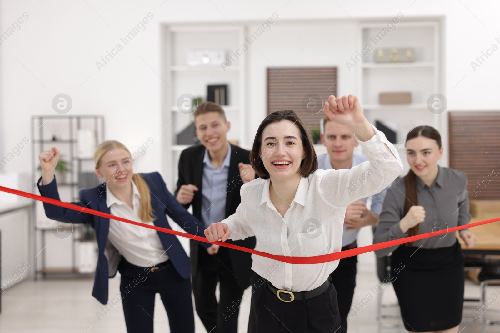 Photo of Competition concept. Happy businesswoman crossing red finish line ahead of her colleagues in office