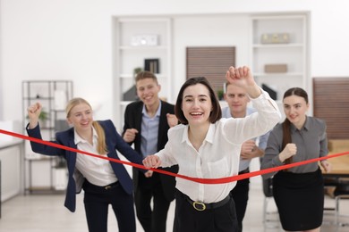 Competition concept. Happy businesswoman crossing red finish line ahead of her colleagues in office