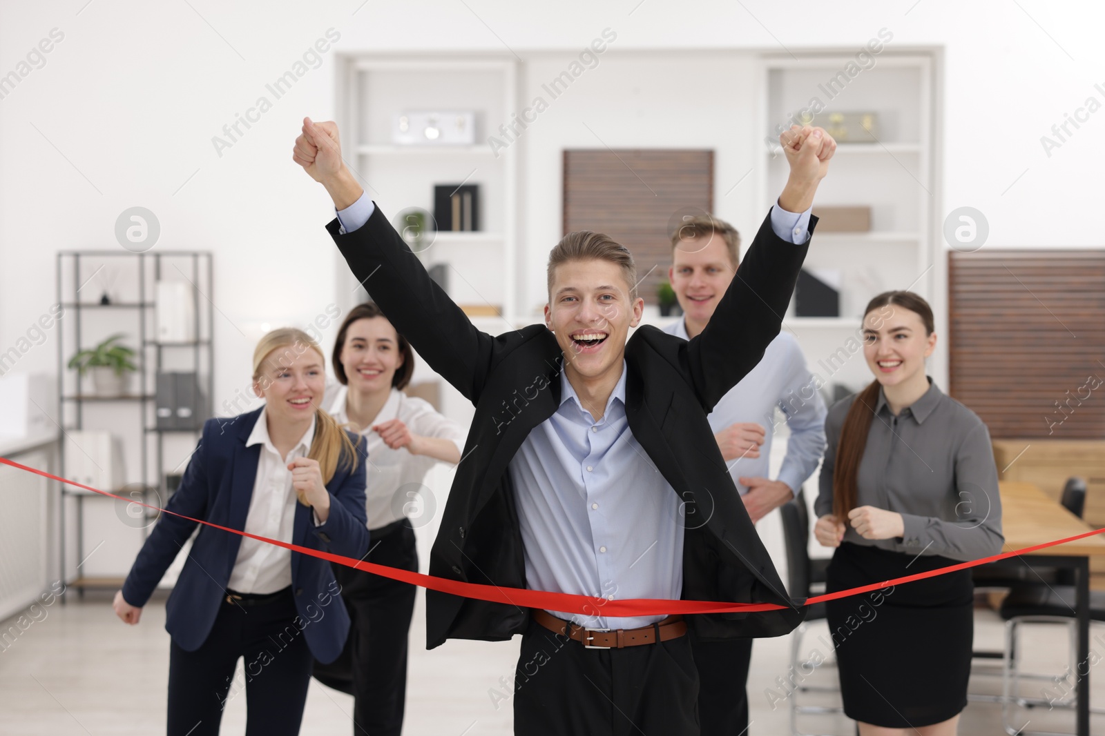 Photo of Competition concept. Happy businessman crossing red finish line ahead of his colleagues in office