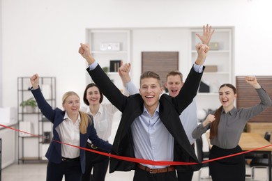 Competition concept. Happy businessman crossing red finish line ahead of his colleagues in office