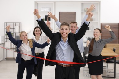 Photo of Competition concept. Happy businessman crossing red finish line ahead of his colleagues in office