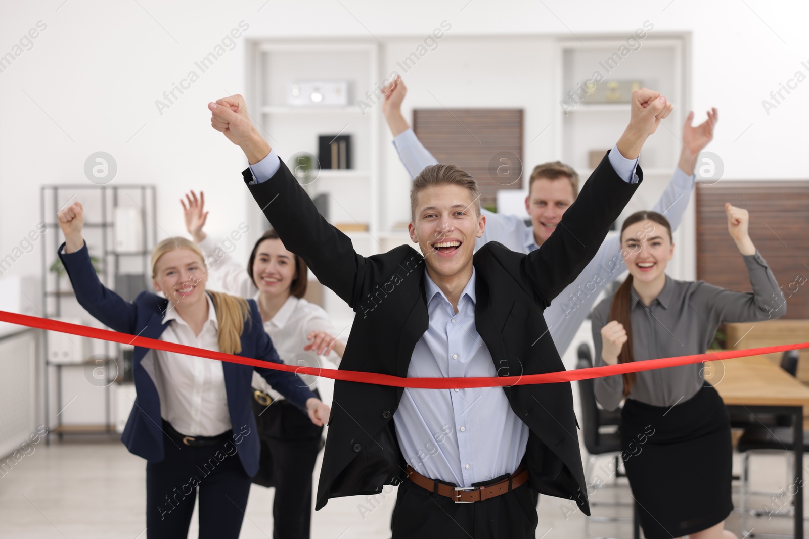 Photo of Competition concept. Happy businessman crossing red finish line ahead of his colleagues in office