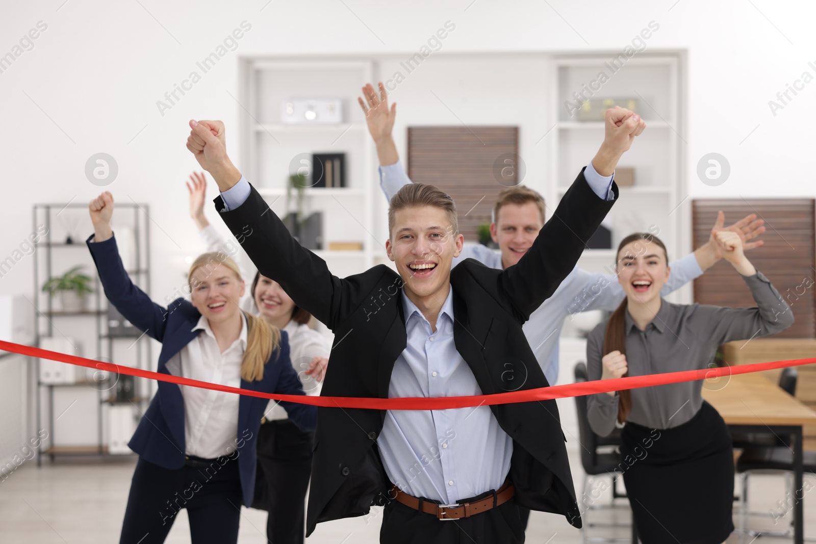 Photo of Competition concept. Happy businessman crossing red finish line ahead of his colleagues in office