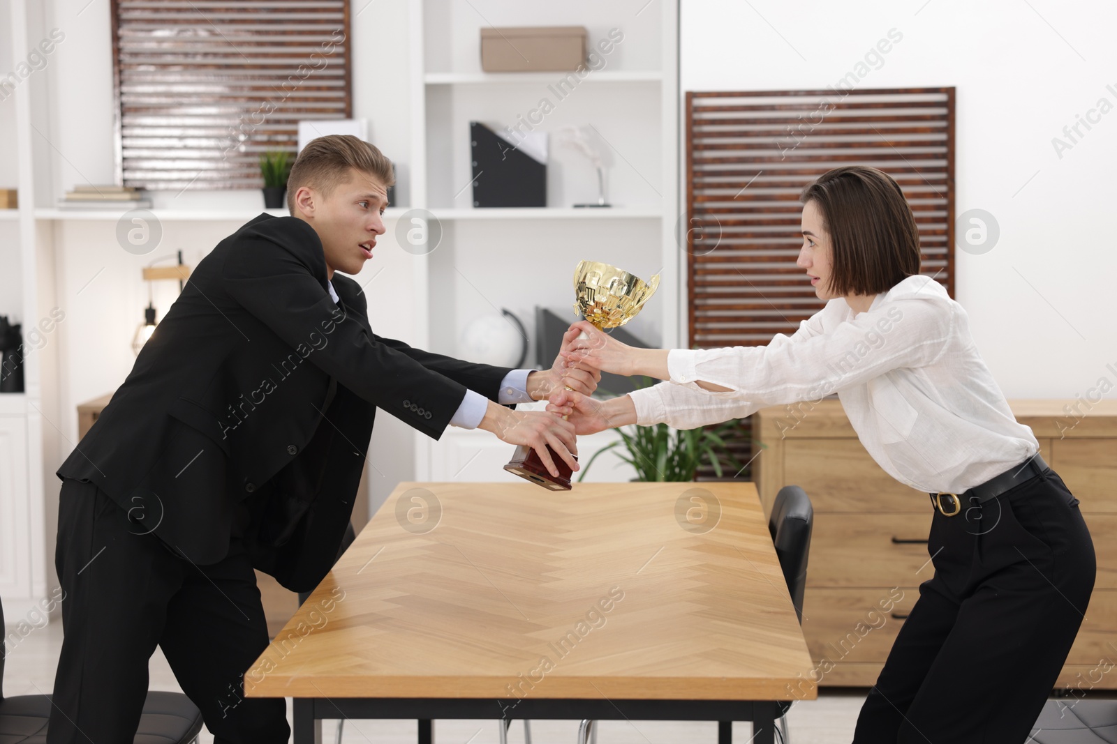 Photo of Business competition. Colleagues pulling golden trophy at table in office