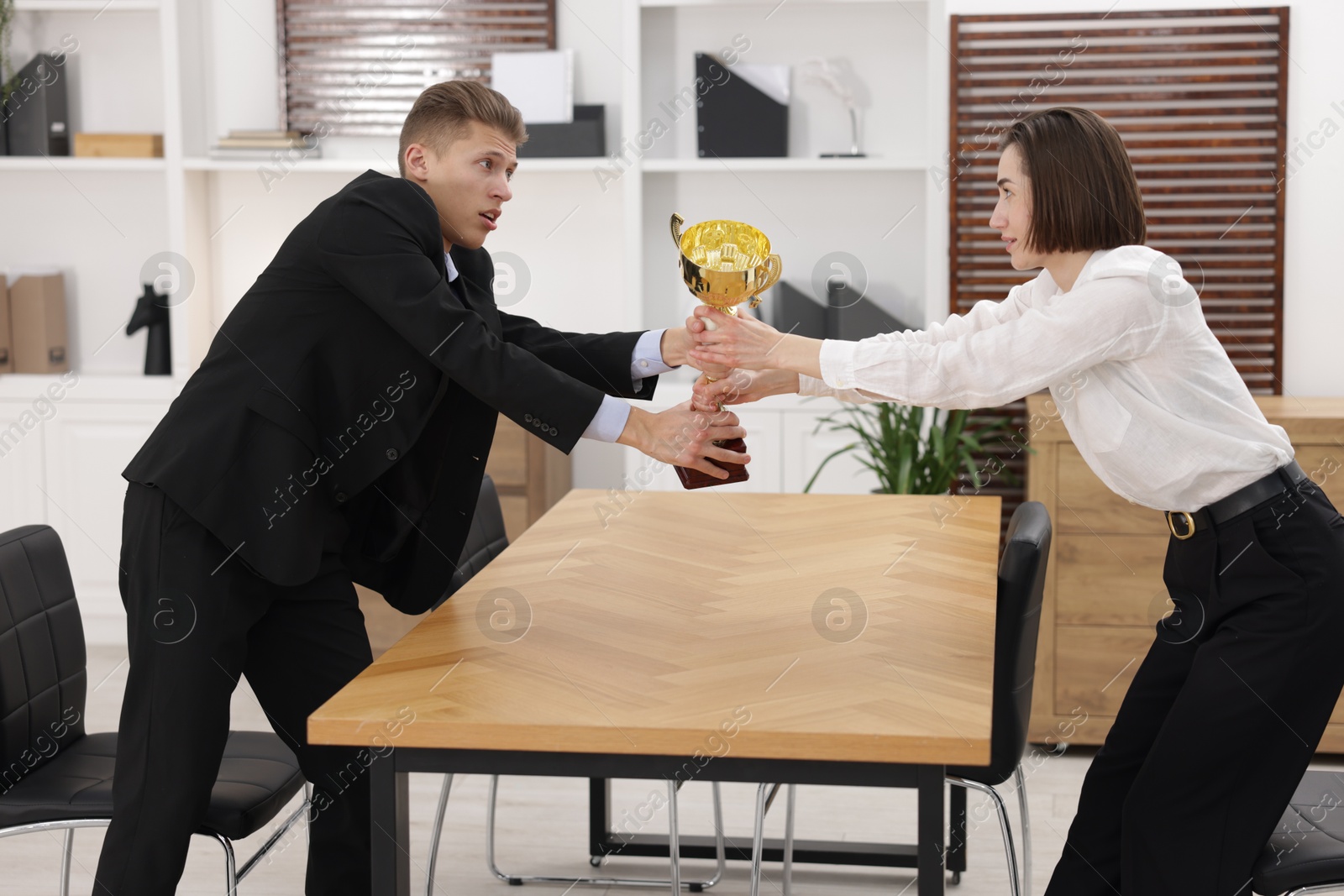 Photo of Business competition. Colleagues pulling golden trophy at table in office