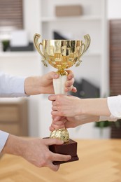 Business competition. Colleagues pulling golden trophy in office, closeup