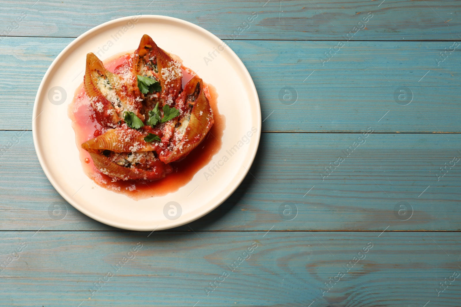 Photo of Delicious conchiglie pasta with ricotta cheese, tomato sauce and parsley on light blue wooden table, top view. Space for text