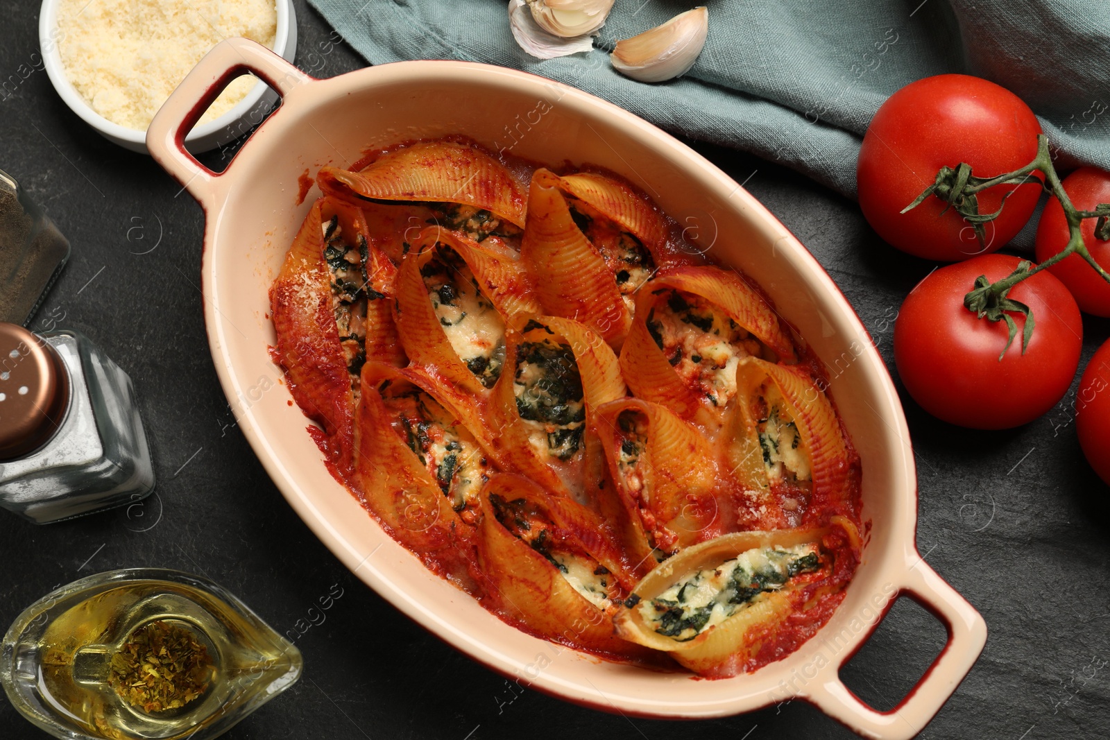 Photo of Delicious conchiglie pasta with ricotta cheese, spinach and tomato sauce in baking dish on black textured table, flat lay