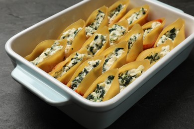 Photo of Delicious conchiglie pasta with ricotta cheese, spinach and tomato sauce in baking dish on black textured table, closeup