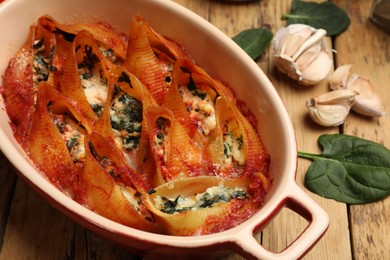 Photo of Delicious conchiglie pasta with ricotta cheese, spinach and tomato sauce in baking dish on wooden table, closeup