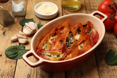 Photo of Delicious conchiglie pasta with ricotta cheese, spinach and tomato sauce in baking dish on wooden table, closeup