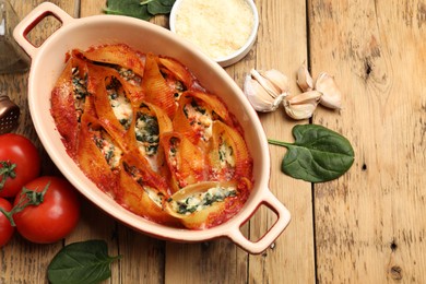 Photo of Delicious conchiglie pasta with ricotta cheese, spinach and tomato sauce in baking dish on wooden table, flat lay