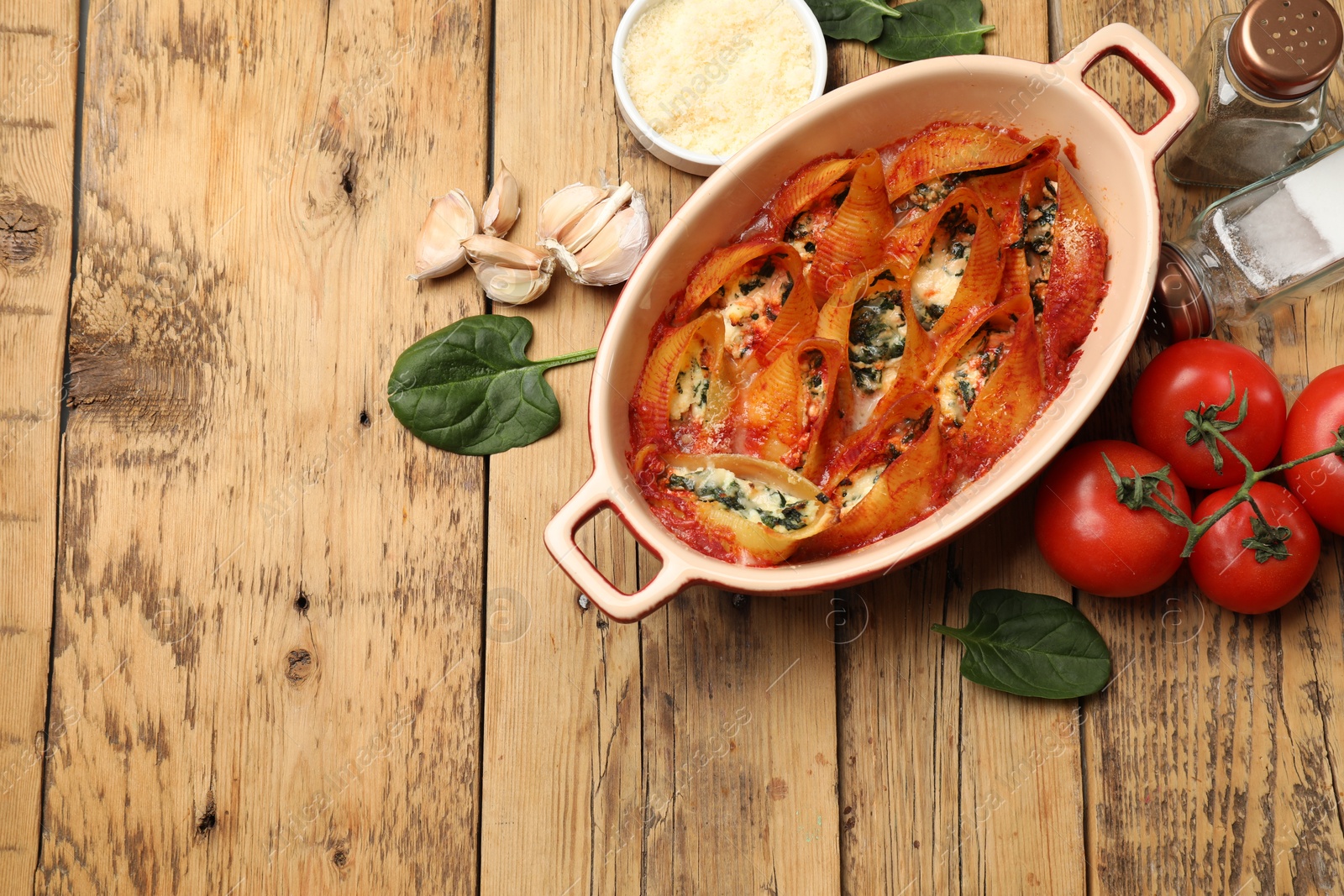 Photo of Delicious conchiglie pasta with ricotta cheese, spinach and tomato sauce in baking dish on wooden table, flat lay. Space for text