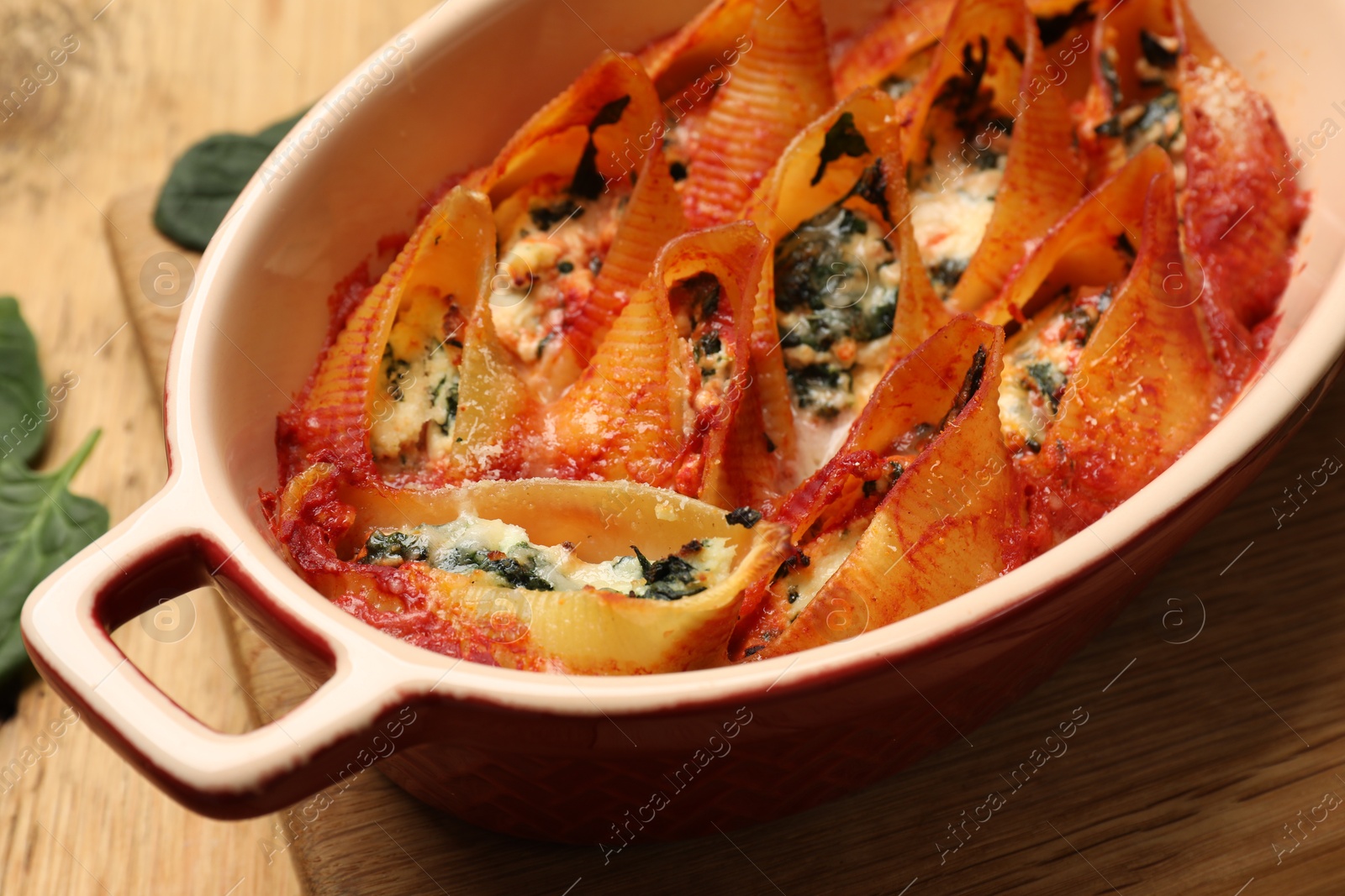 Photo of Delicious conchiglie pasta with ricotta cheese, spinach and tomato sauce in baking dish on table, closeup