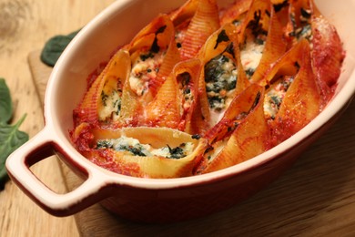 Photo of Delicious conchiglie pasta with ricotta cheese, spinach and tomato sauce in baking dish on table, closeup