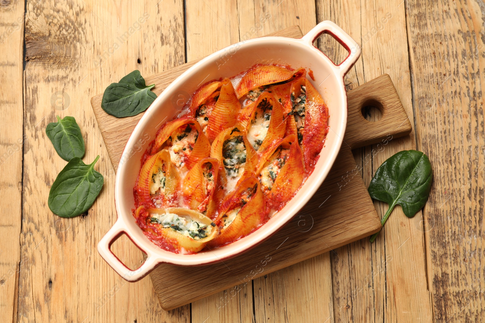 Photo of Delicious conchiglie pasta with ricotta cheese, spinach and tomato sauce in baking dish on wooden table, top view