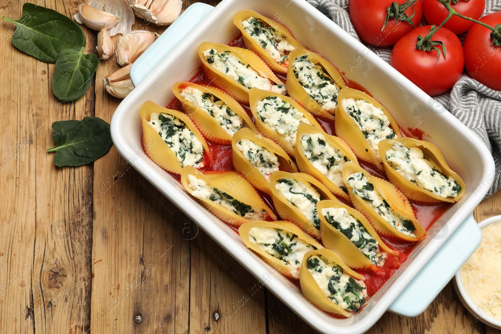 Photo of Delicious conchiglie pasta with ricotta cheese, spinach and tomato sauce in baking dish on wooden table, flat lay