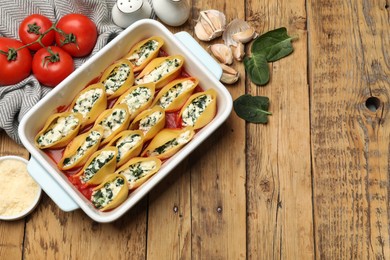 Photo of Delicious conchiglie pasta with ricotta cheese, spinach and tomato sauce in baking dish on wooden table, flat lay. Space for text