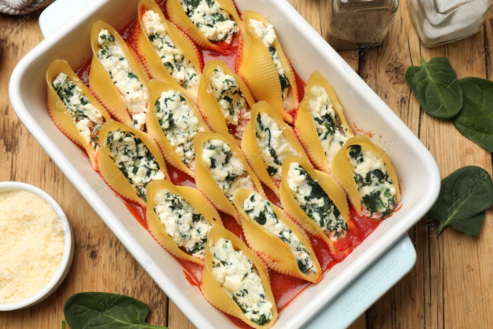 Photo of Delicious conchiglie pasta with ricotta cheese, spinach and tomato sauce in baking dish on wooden table, flat lay