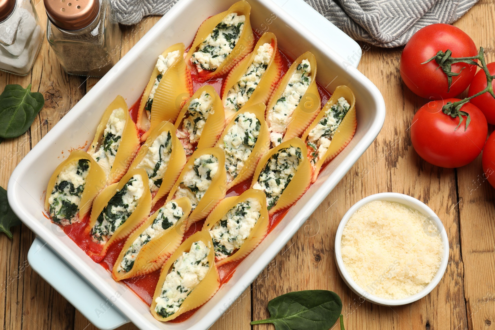 Photo of Delicious conchiglie pasta with ricotta cheese, spinach and tomato sauce in baking dish on wooden table, flat lay