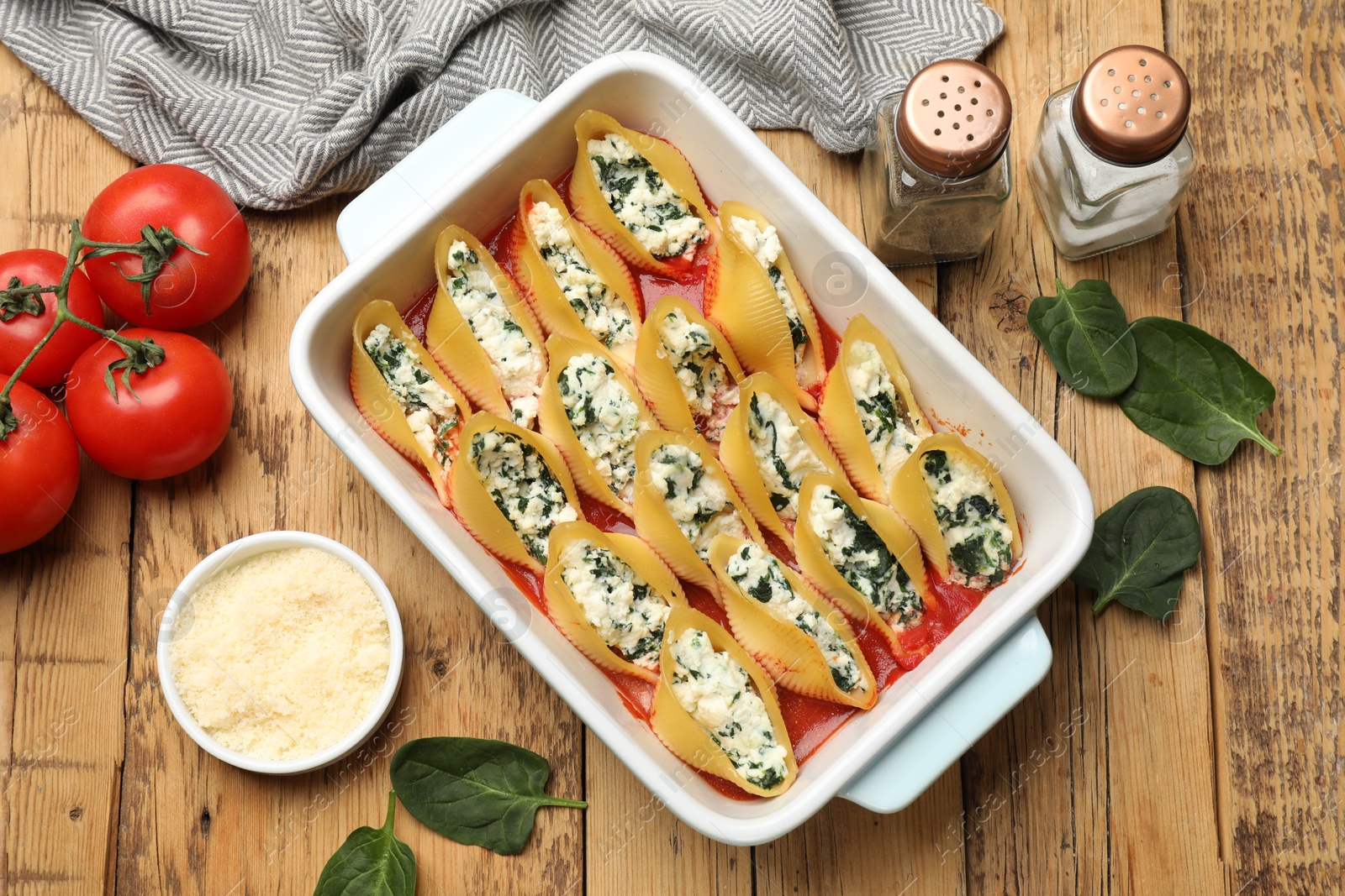 Photo of Delicious conchiglie pasta with ricotta cheese, spinach and tomato sauce in baking dish on wooden table, flat lay