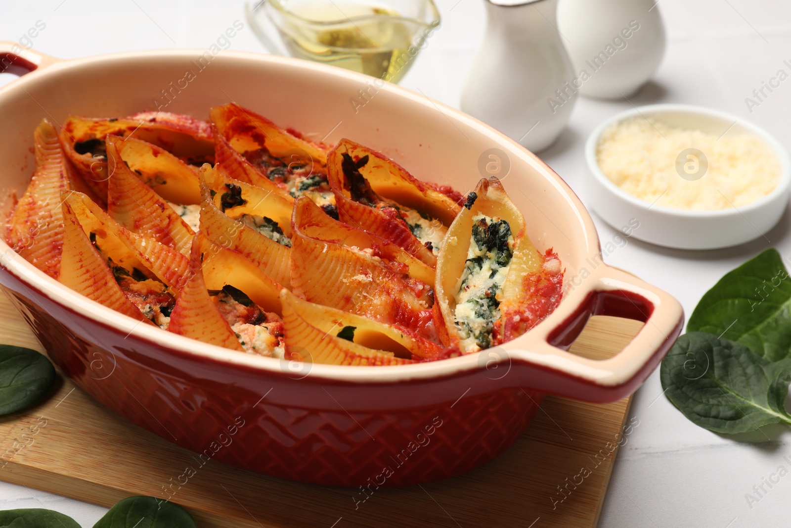 Photo of Delicious conchiglie pasta with ricotta cheese, spinach and tomato sauce in baking dish on light table, closeup