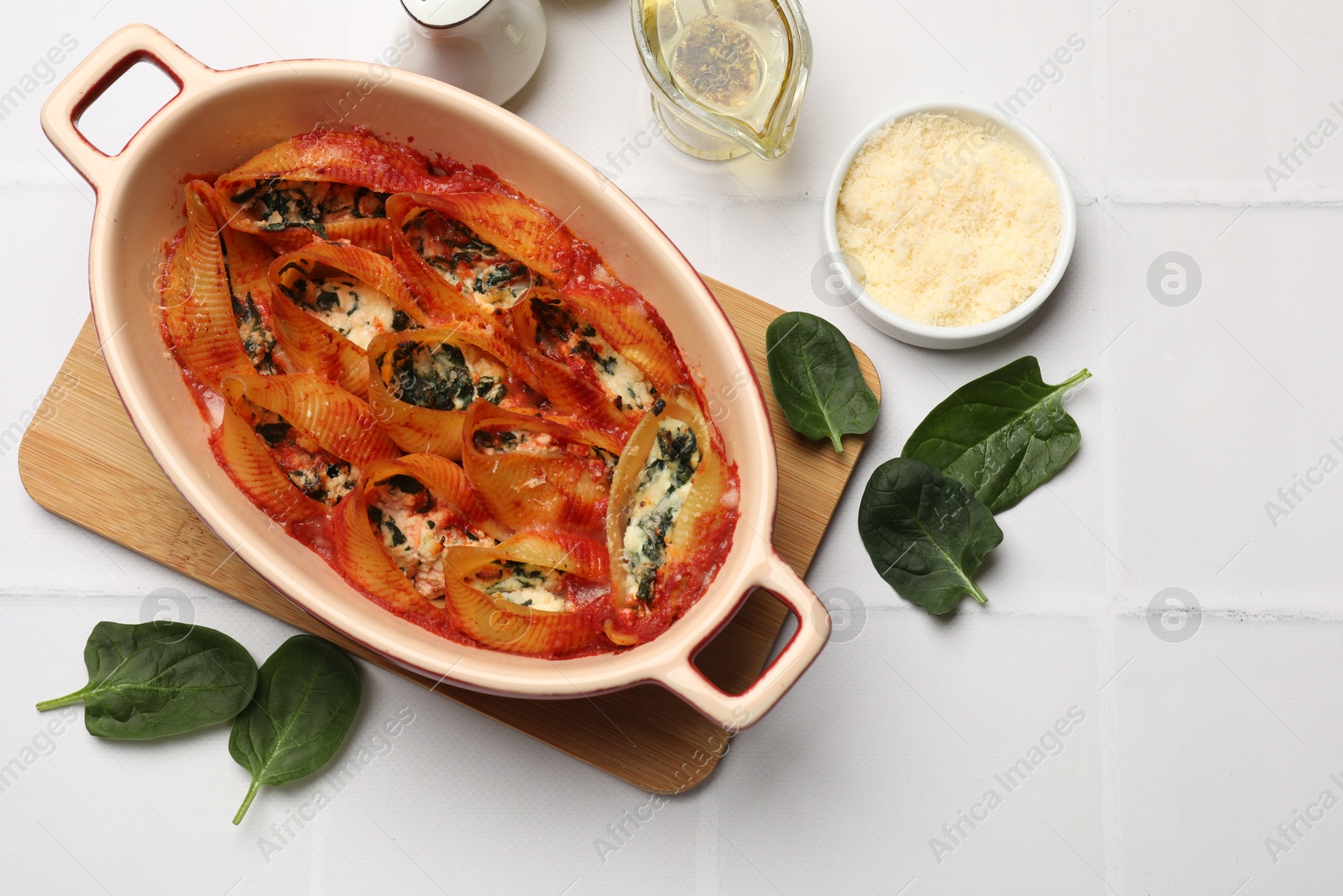 Photo of Delicious conchiglie pasta with ricotta cheese, spinach and tomato sauce in baking dish on white tiled table, flat lay