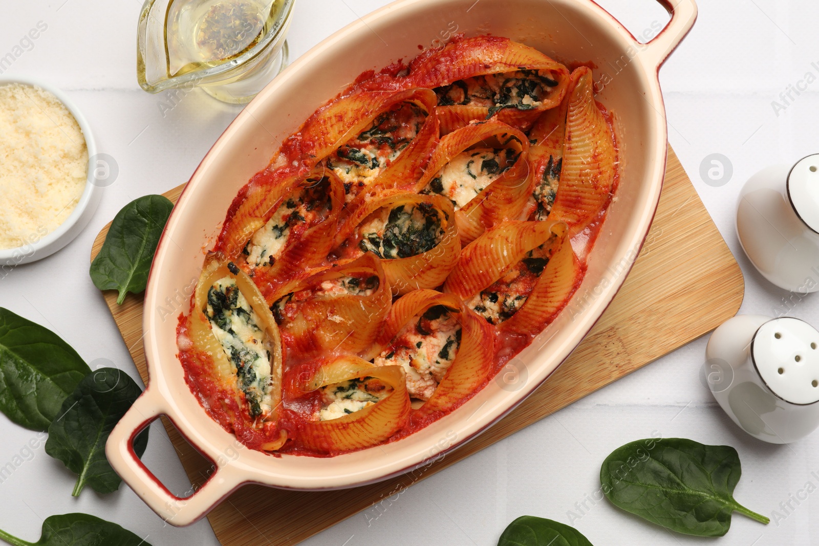 Photo of Delicious conchiglie pasta with ricotta cheese, spinach and tomato sauce in baking dish on white table, flat lay