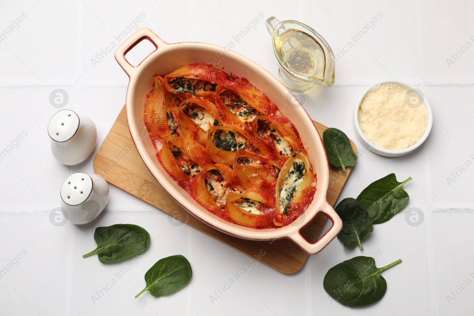 Photo of Delicious conchiglie pasta with ricotta cheese, spinach and tomato sauce in baking dish on white tiled table, flat lay