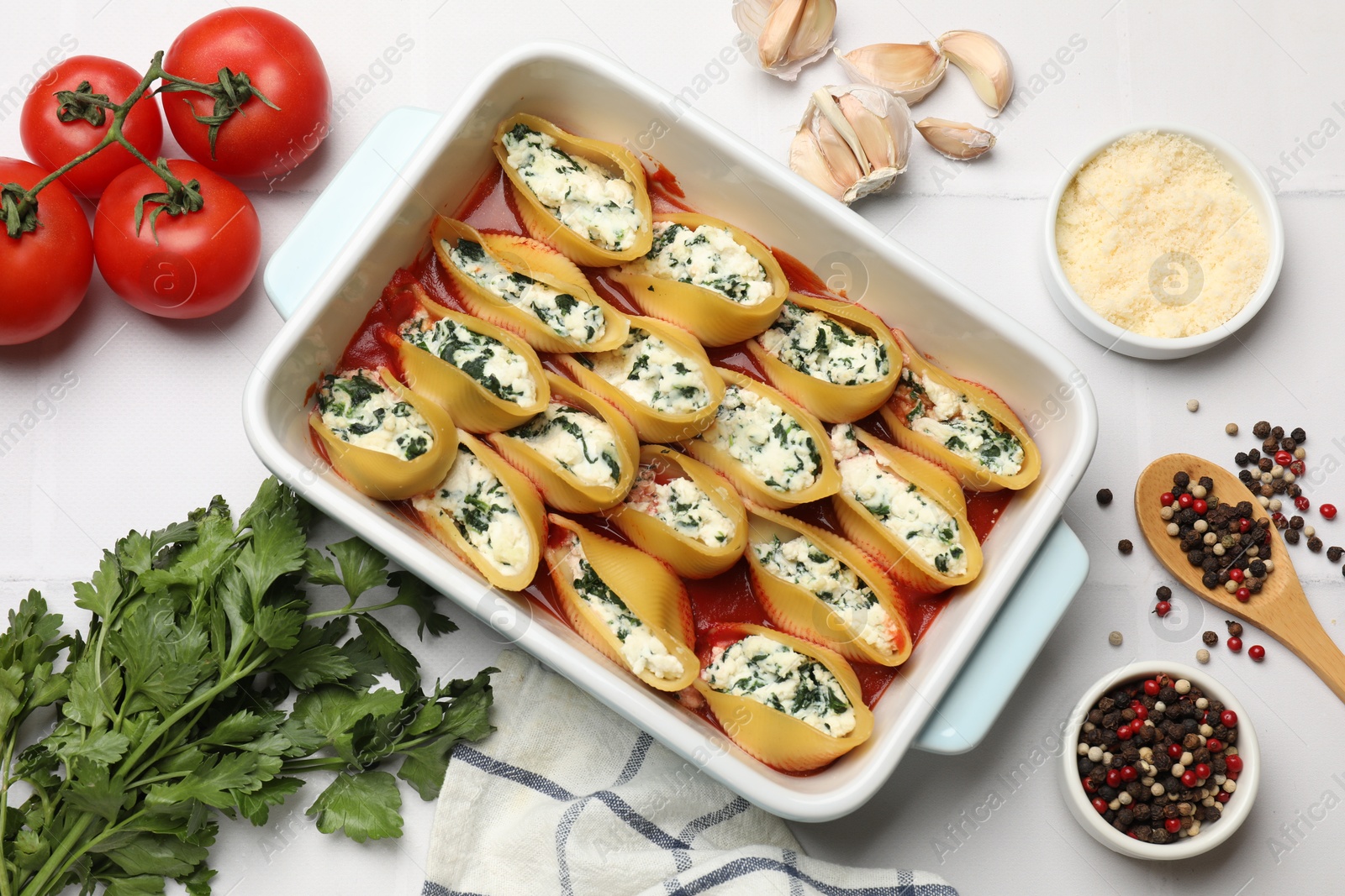 Photo of Delicious conchiglie pasta with ricotta cheese, spinach and tomato sauce in baking dish on white table, flat lay